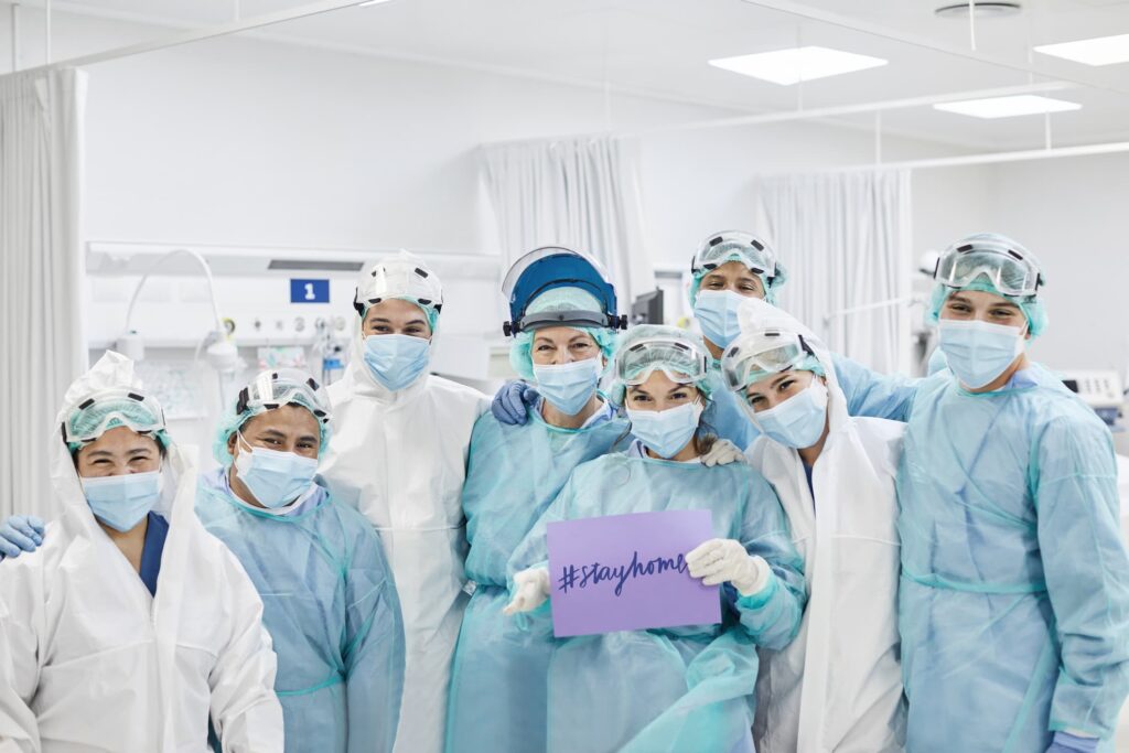 Frontline workers standing in ICU wearing protective workwear holding up sign that says "stay home"